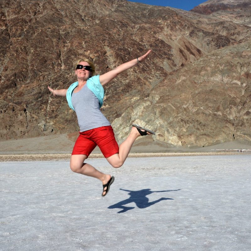 Szabadság a sivatagban – Death Valley kaland Utazó a Death Valley sós medencéjénél a levegőbe ugrik, a tengerszint alatti tájban